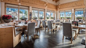 A restaurant with wooden interiors, large windows, and a view of mountains. - Hotel Spitzhorn (Saanen)