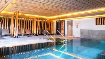 Una piscina con vigas de madera y suelo de baldosas, rodeada de sillones de descanso y un muro de madera.