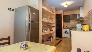 A compact kitchen with a built-in washing machine, a refrigerator, and a dining area with a table. - Résidence Mirador Majorelle (Marrakech)