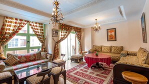 A traditional living room with a sofa set, a glass coffee table, a red table, and a wooden stool. - Résidence Mirador Majorelle (Marrakech)