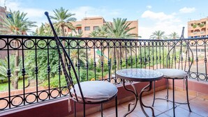 A balcony with two metal chairs and a small round table, overlooking a garden with palm trees and buildings in the background. - Résidence Mirador Majorelle (Marrakech)
