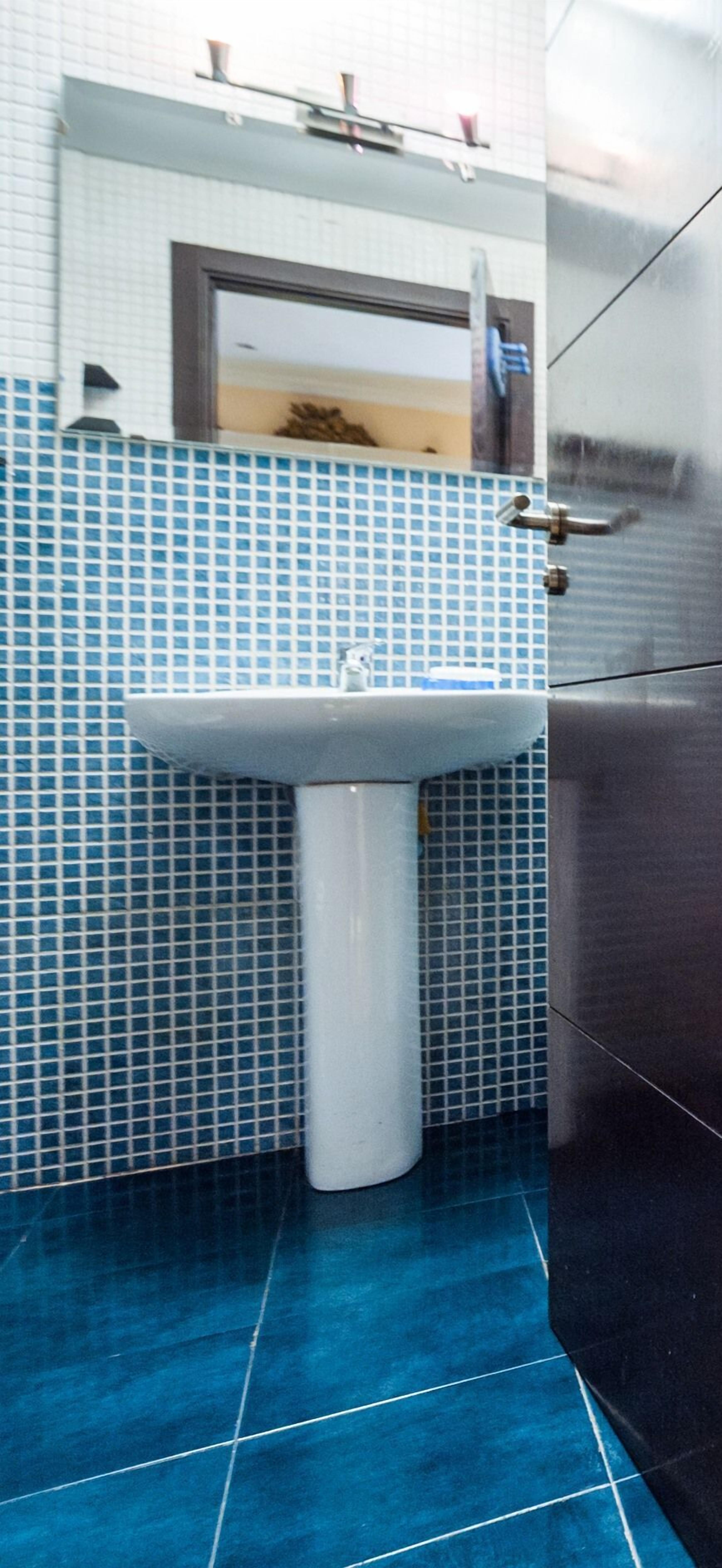 Une salle de bain avec un lavabo blanc, des murs recouverts de carreaux bleus et un sol bleu.