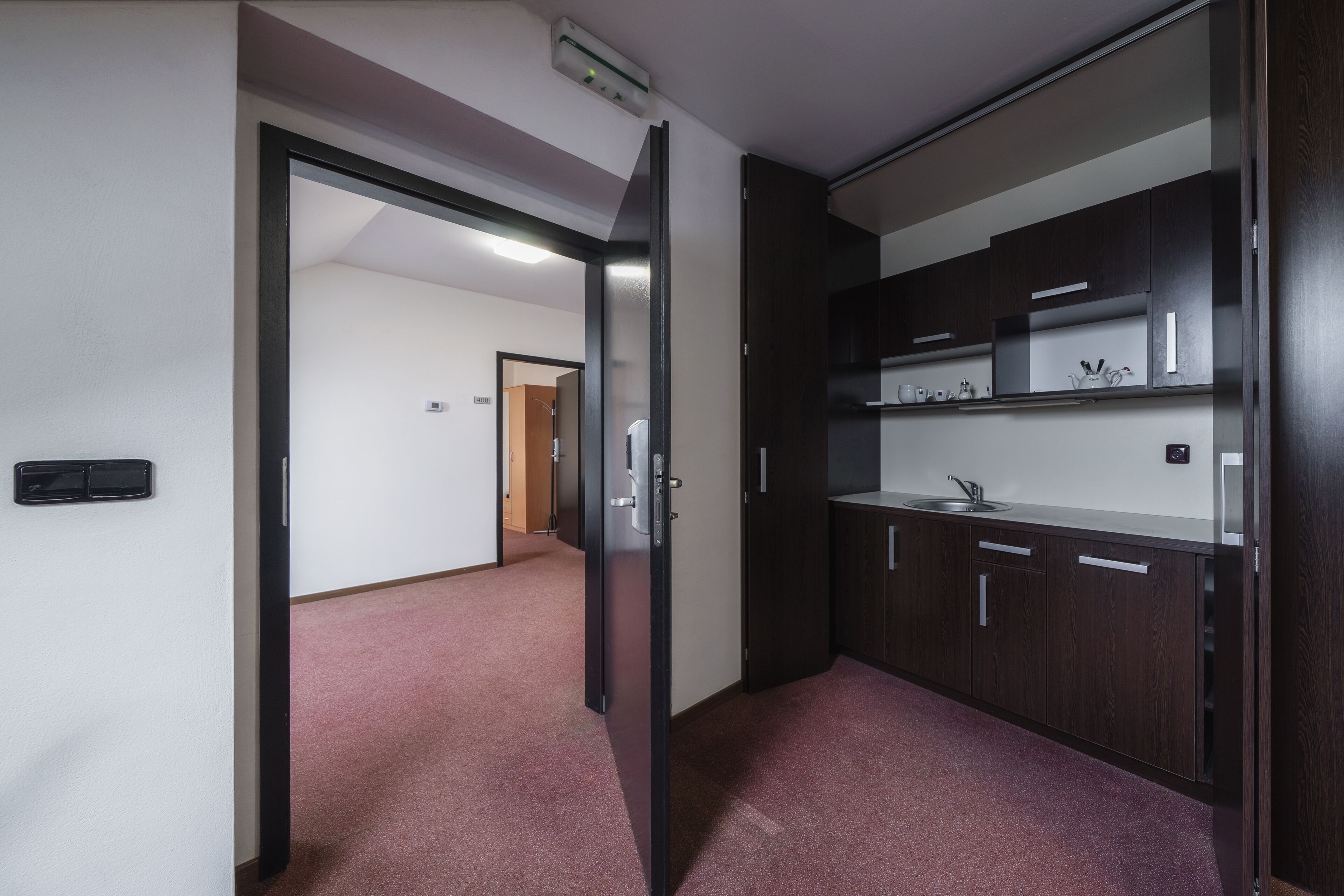 Un pasillo con piso alfombrado, una puerta que da a una cocina con gabinetes de madera oscura y una encimera.