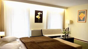 A hotel room with a bed, a sofa, a desk, and a window with curtains. - Astory Hotel (Plzen)