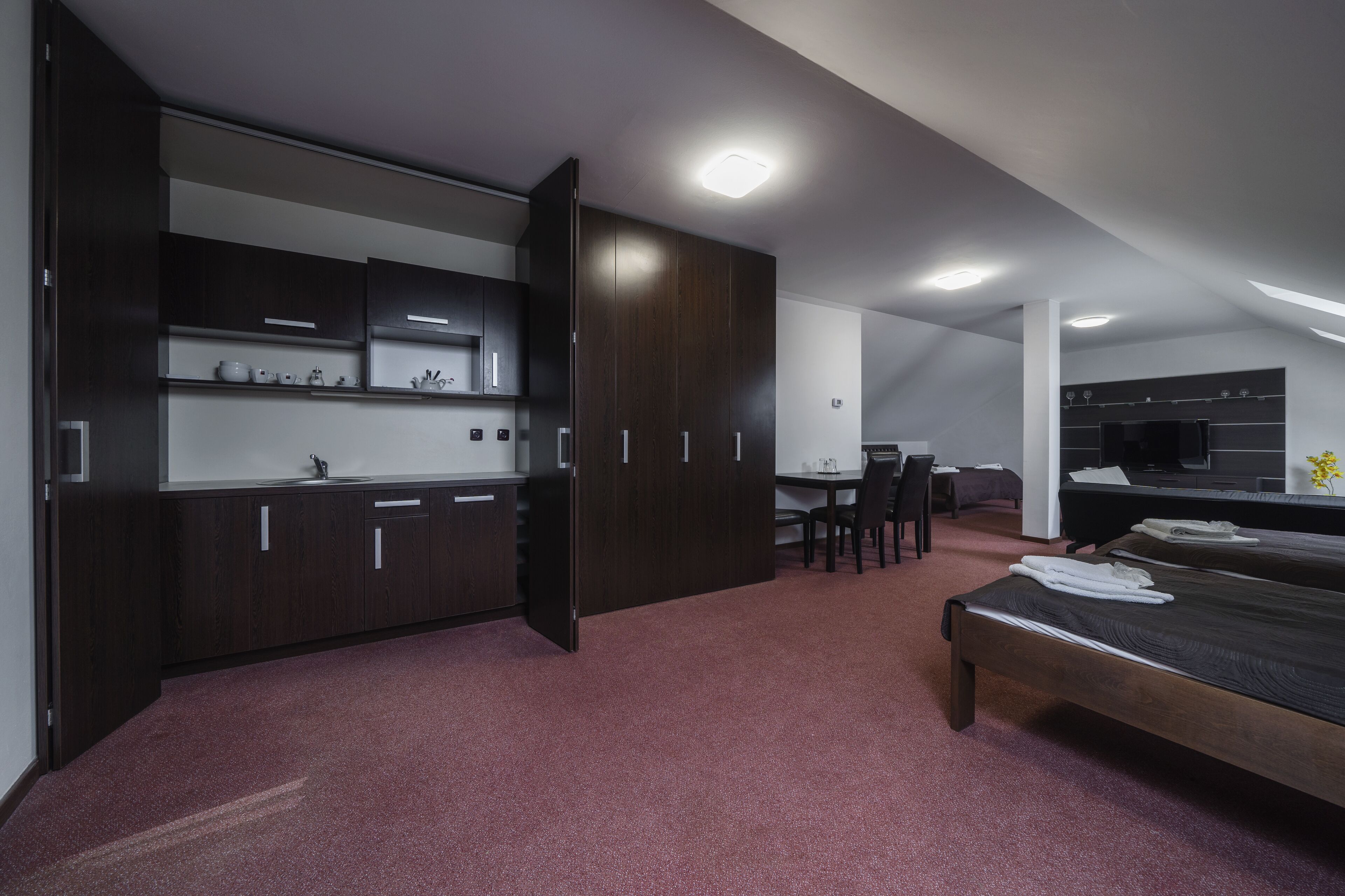 A modern hotel room with a kitchenette, a dining area, and a large bed.