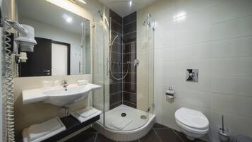 Un baño moderno con ducha de vidrio, un lavamanos blanco y un inodoro.