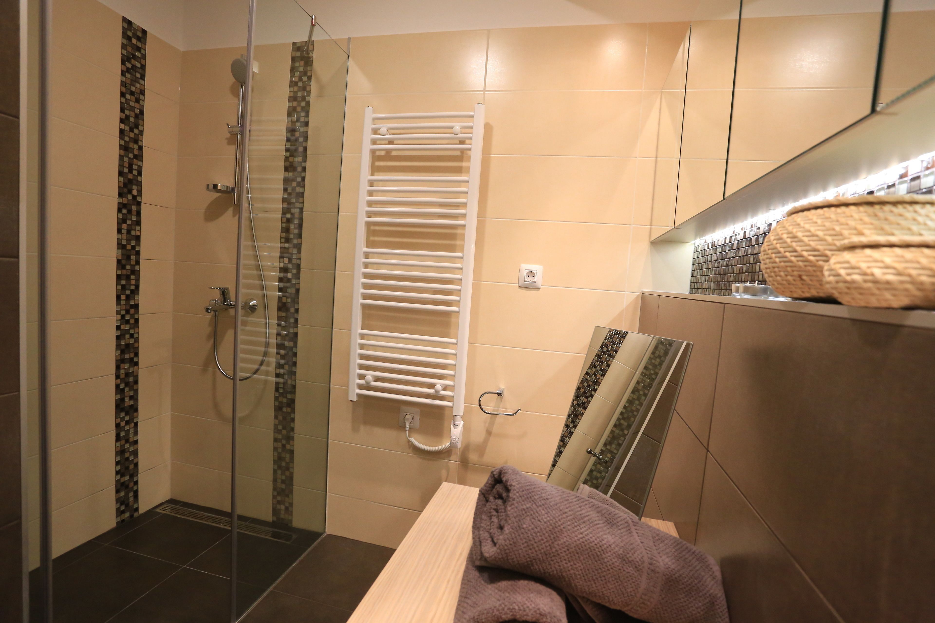 A modern bathroom with a glass shower enclosure, a white towel rack, and a wooden vanity with a towel.