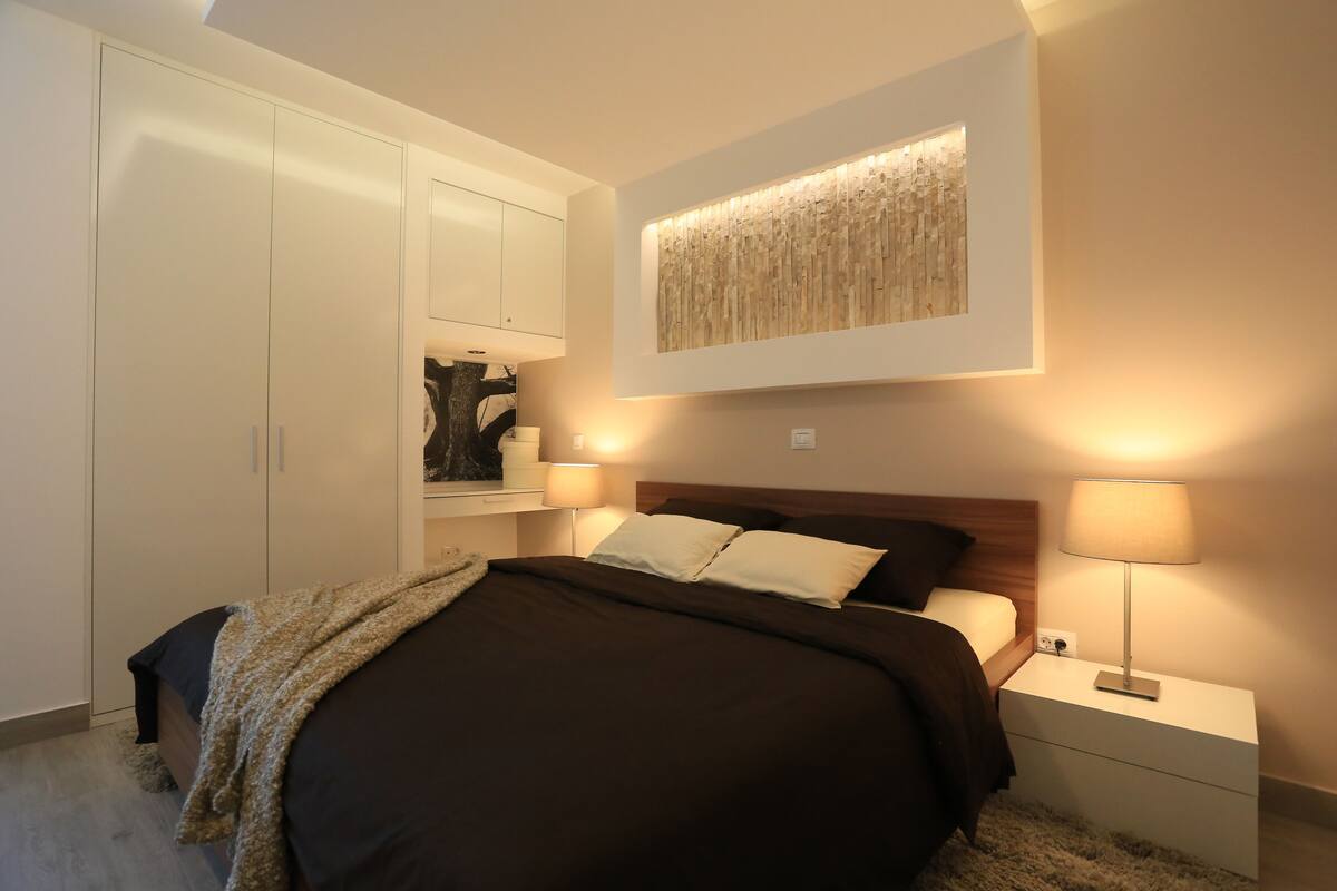 A bedroom with a bed, nightstands, a wall-mounted artwork, and a wardrobe.