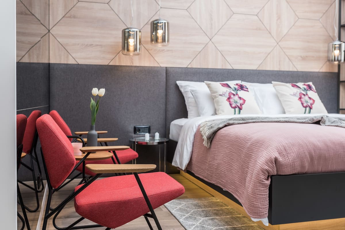 A modern bedroom with a bed, red chairs, a small table, and a vase with flowers.