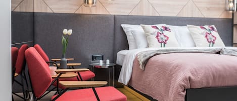 Un dormitorio moderno con cama, sillas rojas, una mesita y un jarrón con flores.