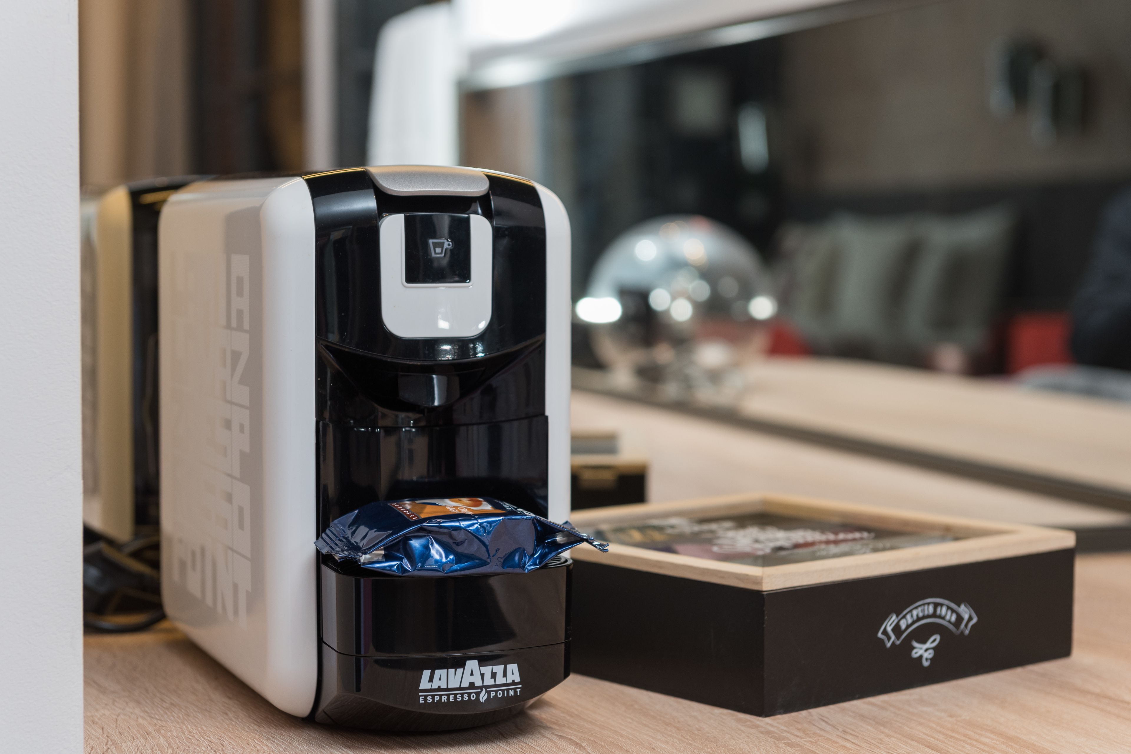 Eine Kaffeemaschine mit einer mit 'Lavazza Espresso Point' beschrifteten Box auf einer Holztischplatte.