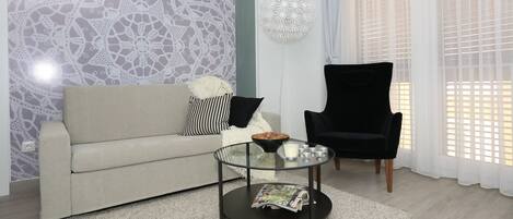 A living room with a sofa, a glass coffee table, a black armchair, and a decorative wall piece.