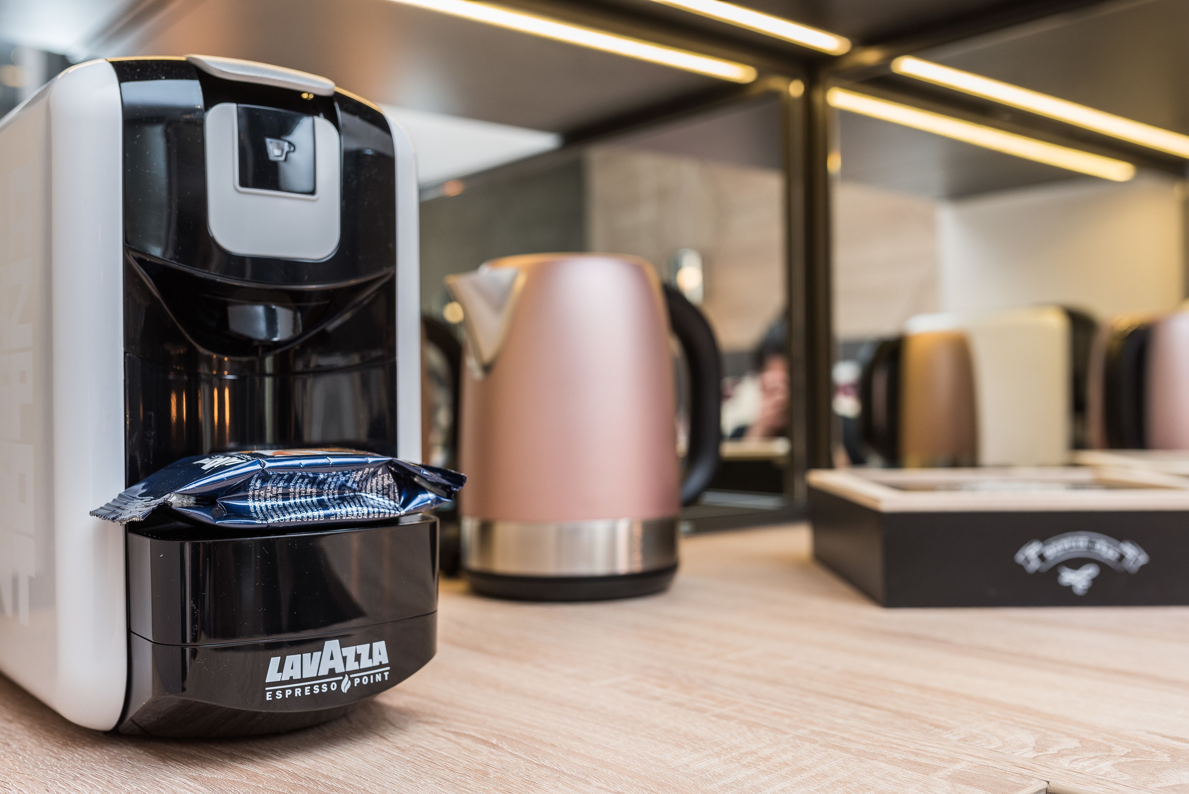 A coffee machine with a black and white design, a stainless steel water carafe, and a branded box on a wooden surface.