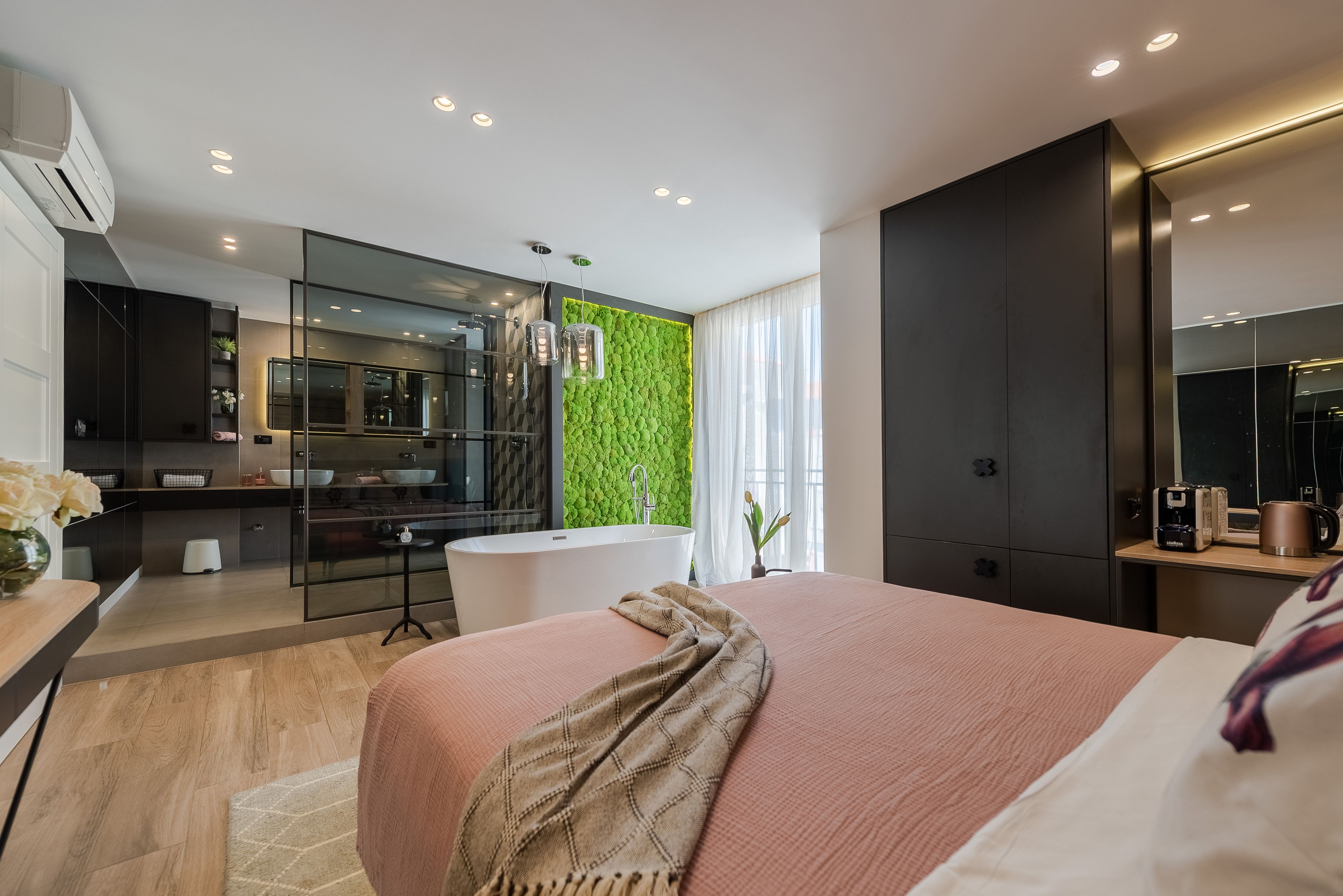 Ein modernes Schlafzimmer mit einem großen Bett, einer grünen Akzentwand, einem Badezimmer mit einer Badewanne und einem großen Spiegel.
