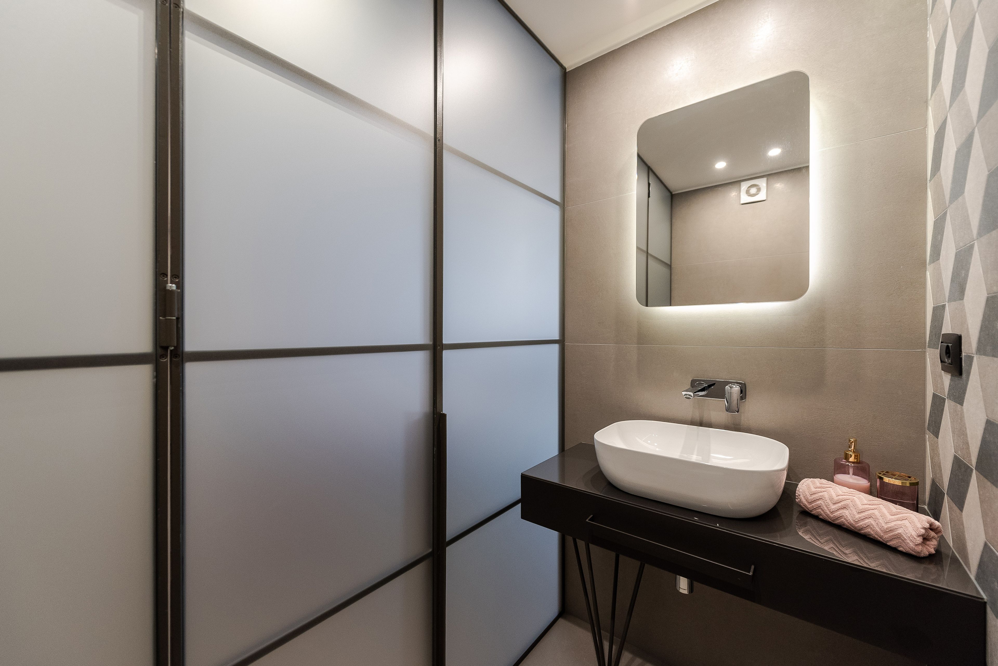 A modern bathroom with a large mirror, a white sink, and a towel on the counter.