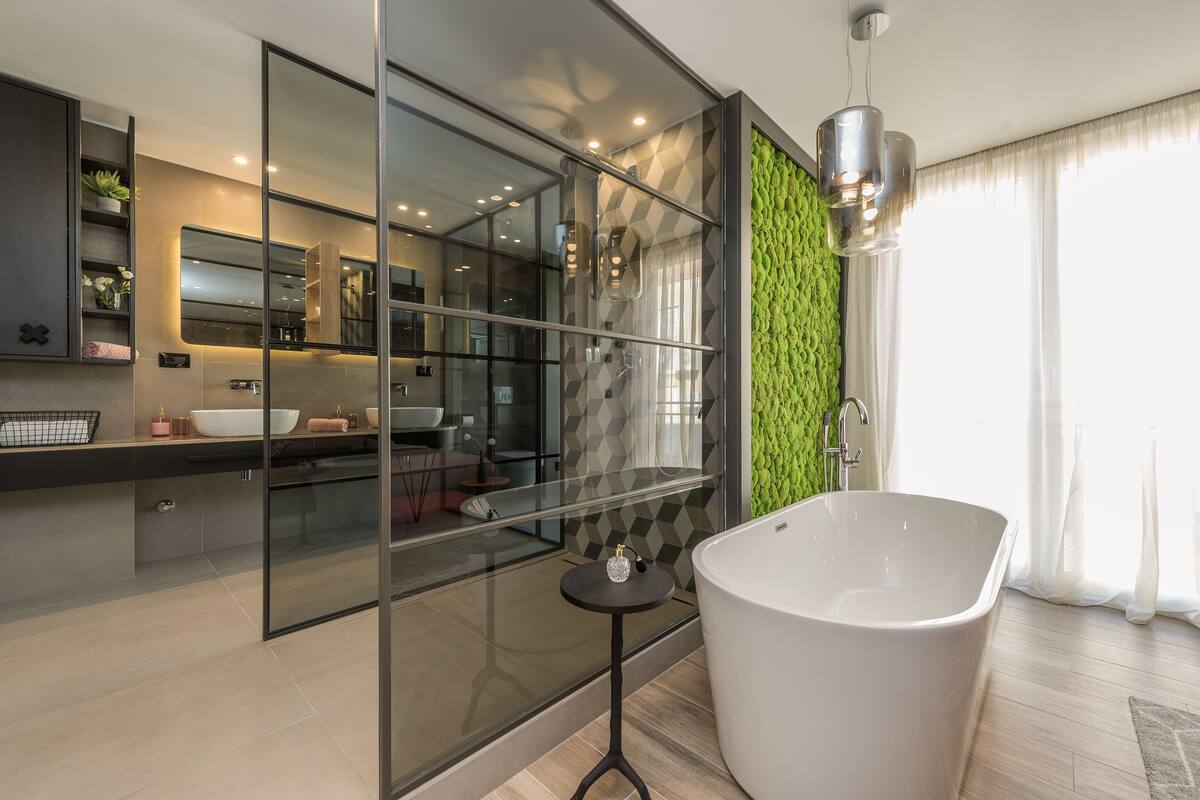 A modern bathroom with a freestanding bathtub, a glass shower enclosure, and a green textured wall.