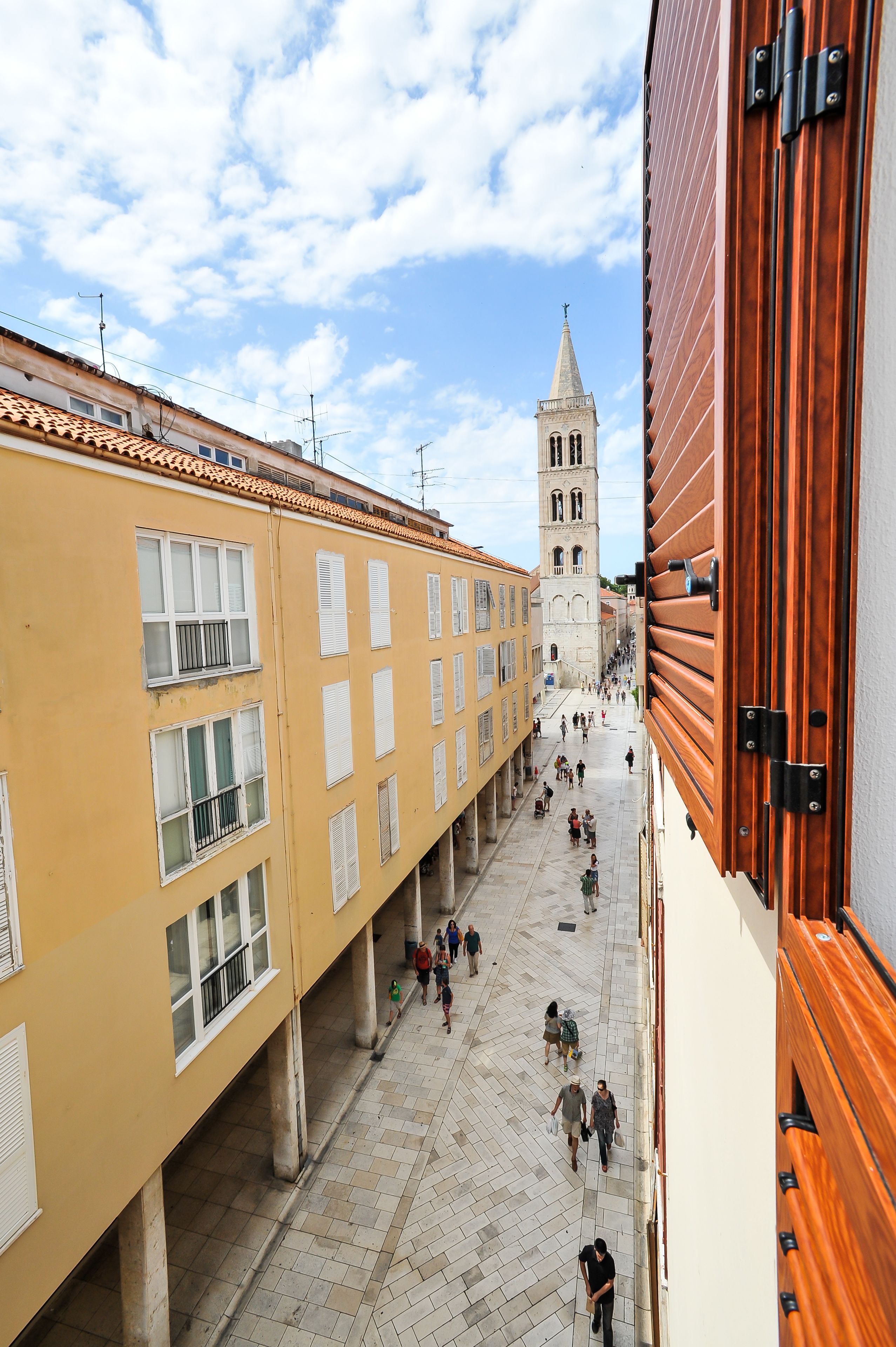 A pedestrian street with buildings on either side, a tower in the background, and a wooden structure on the right.
