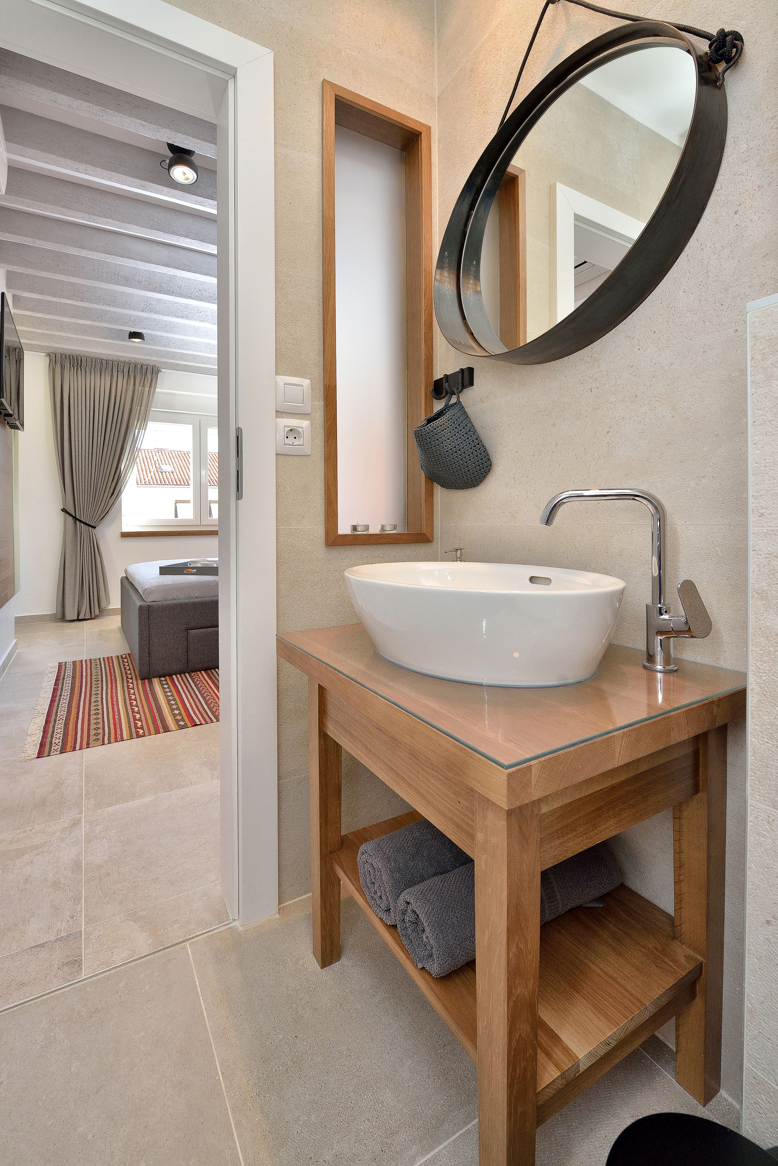 A modern bathroom with a large round mirror, a white sink, and a wooden vanity.