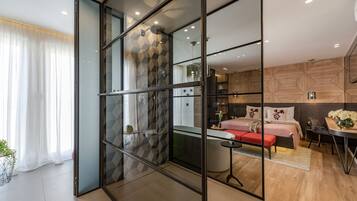 Un dormitorio moderno con un separador de vidrio, una cama, una mesita de noche y una pequeña zona de estar.