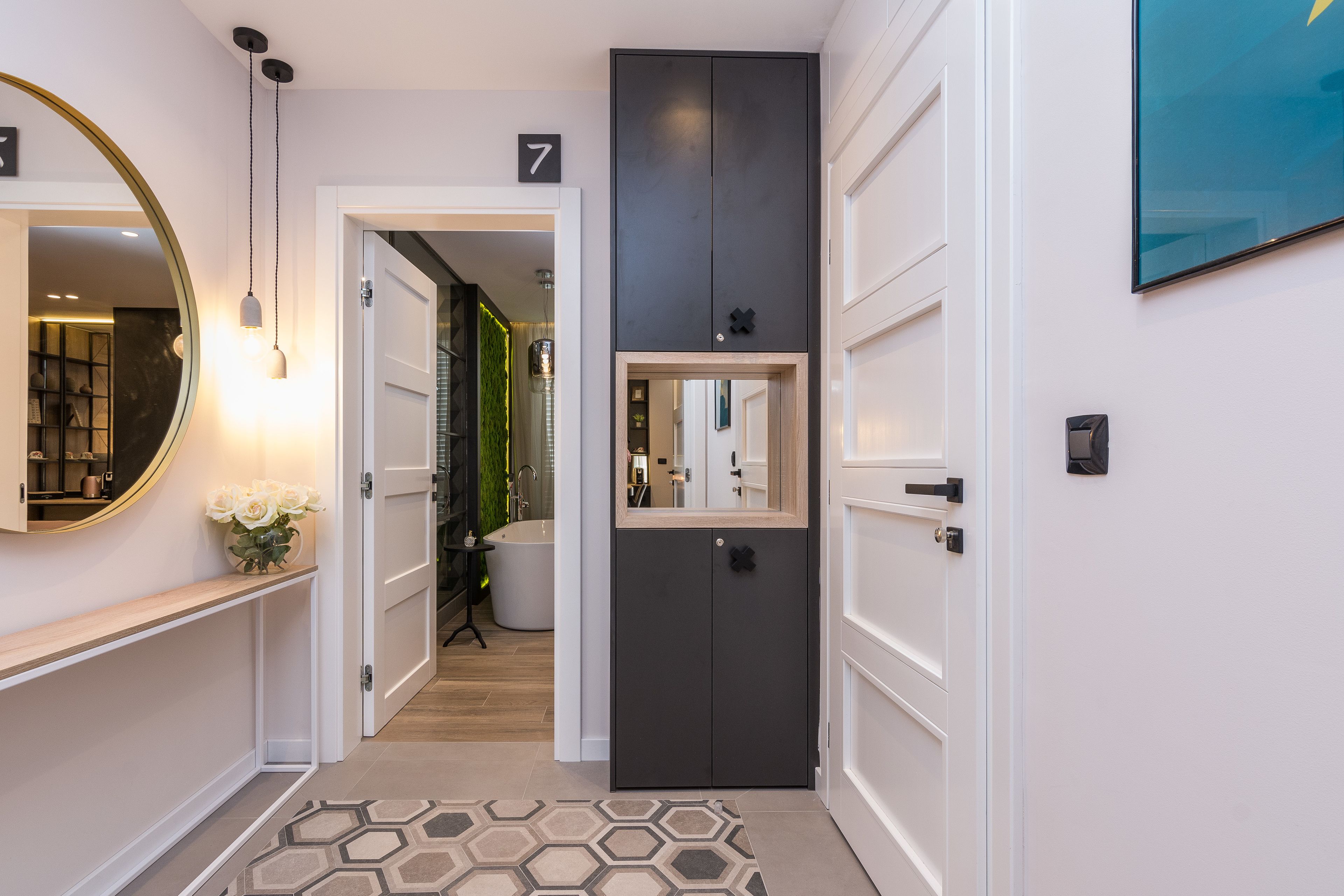 Un couloir avec un miroir, une enseigne portant le chiffre « 7 », un meuble noir et un tapis à motifs hexagonaux.