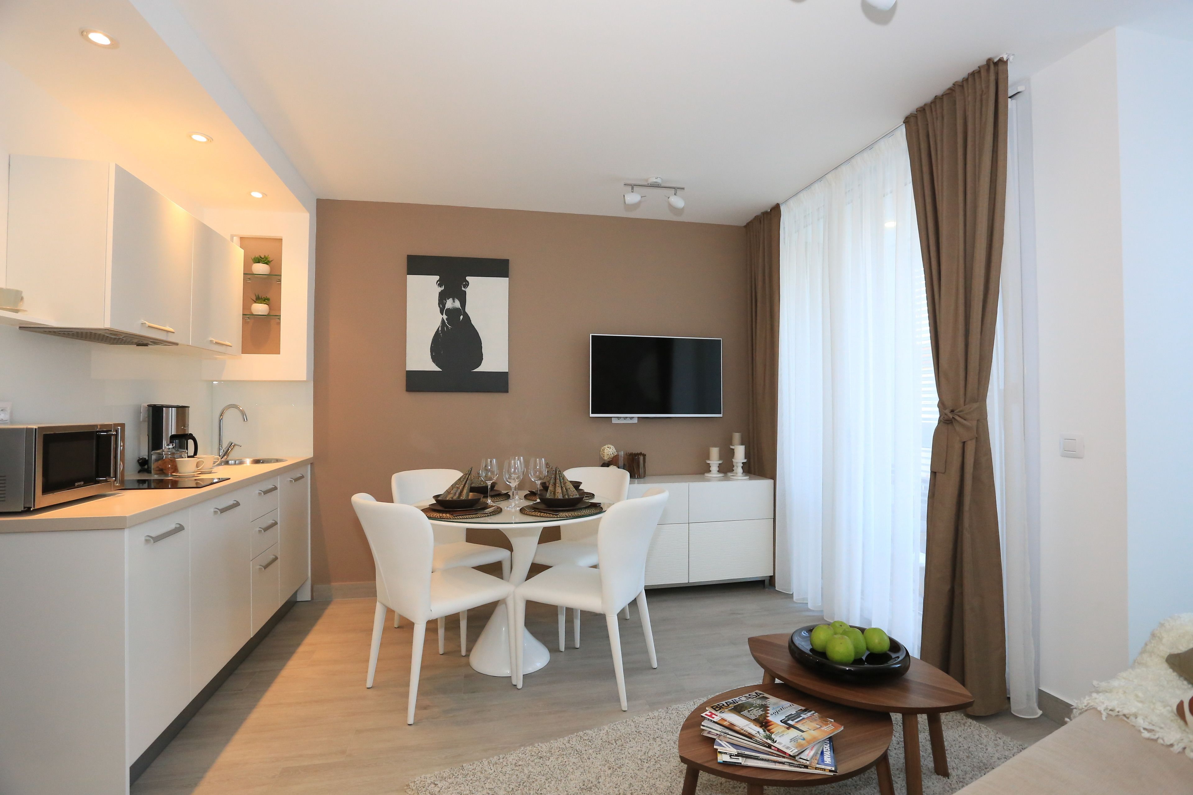 A modern kitchen with white cabinets, a microwave, and a dining area with white chairs and a table set for four.