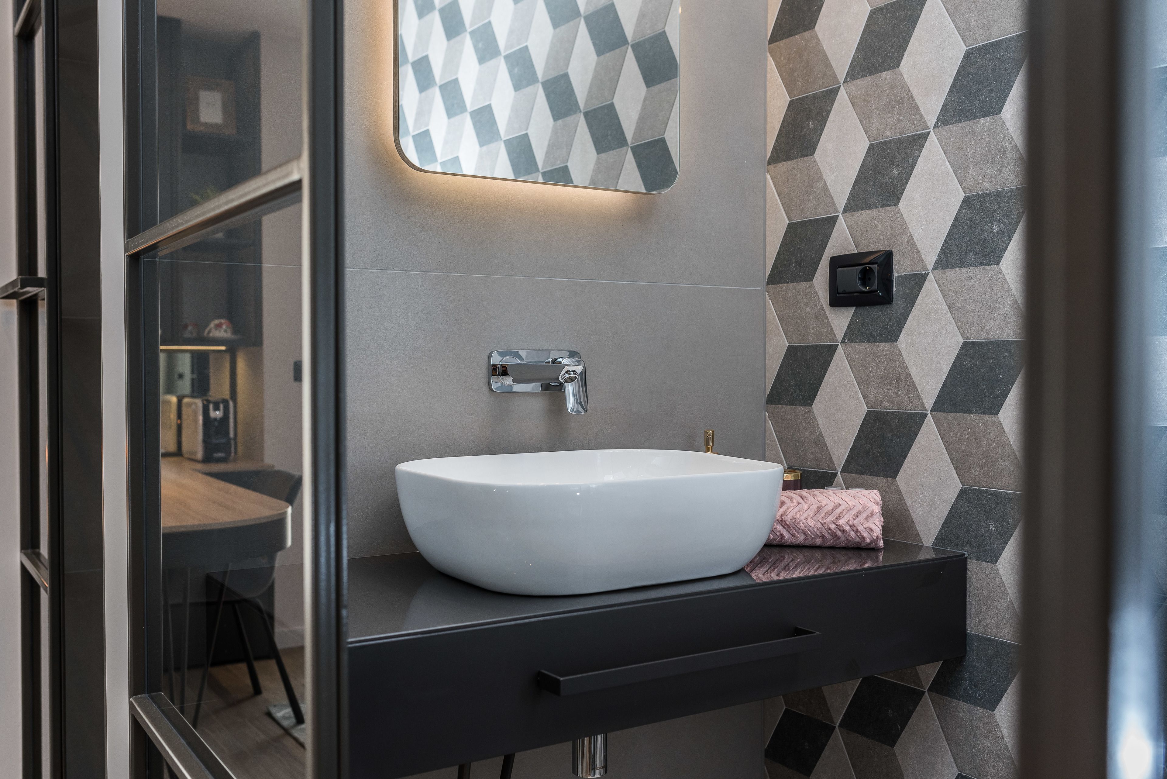 A modern bathroom with a white sink, black countertop, and geometric patterned tiles.