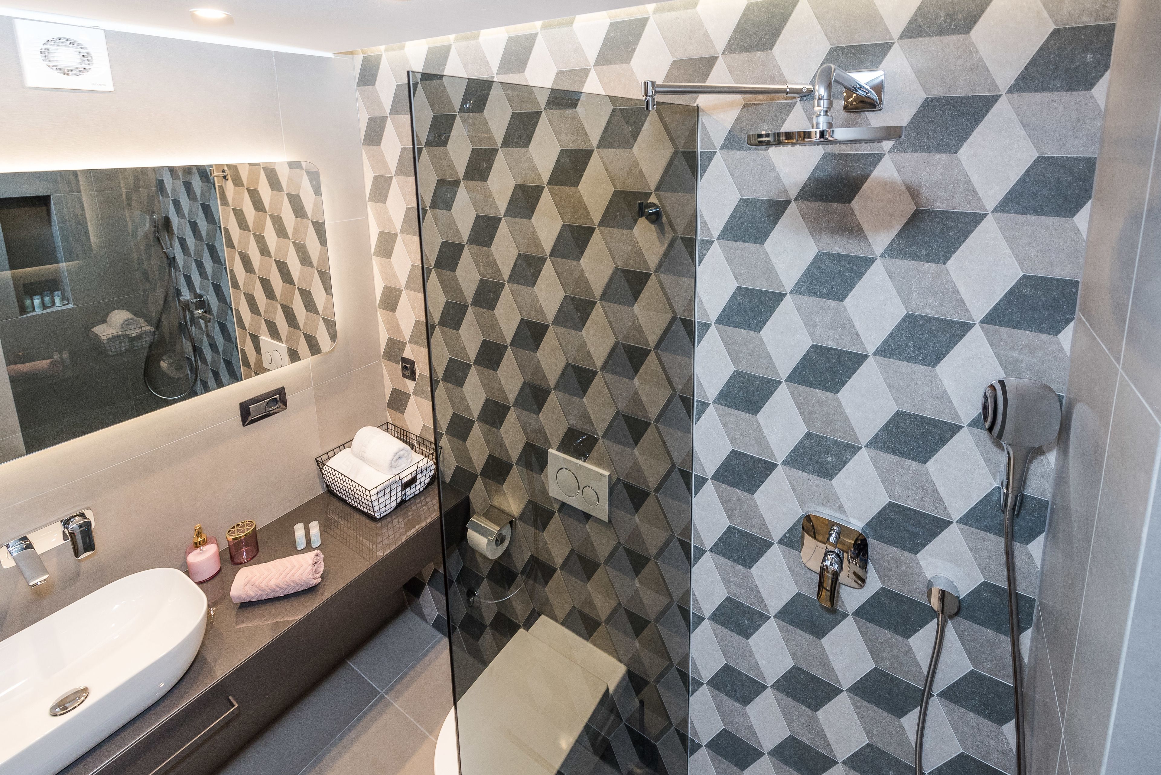 Un baño moderno con un espejo grande, un lavamanos, cabina de ducha de vidrio y pared de azulejos estampados.