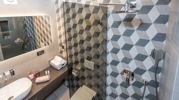 Un baño moderno con un espejo grande, un lavamanos, cabina de ducha de vidrio y pared de azulejos estampados.
