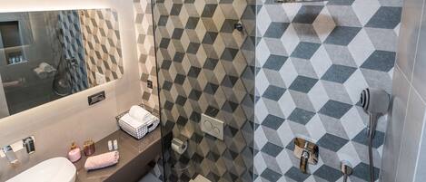 Un baño moderno con un espejo grande, un lavamanos, cabina de ducha de vidrio y pared de azulejos estampados.