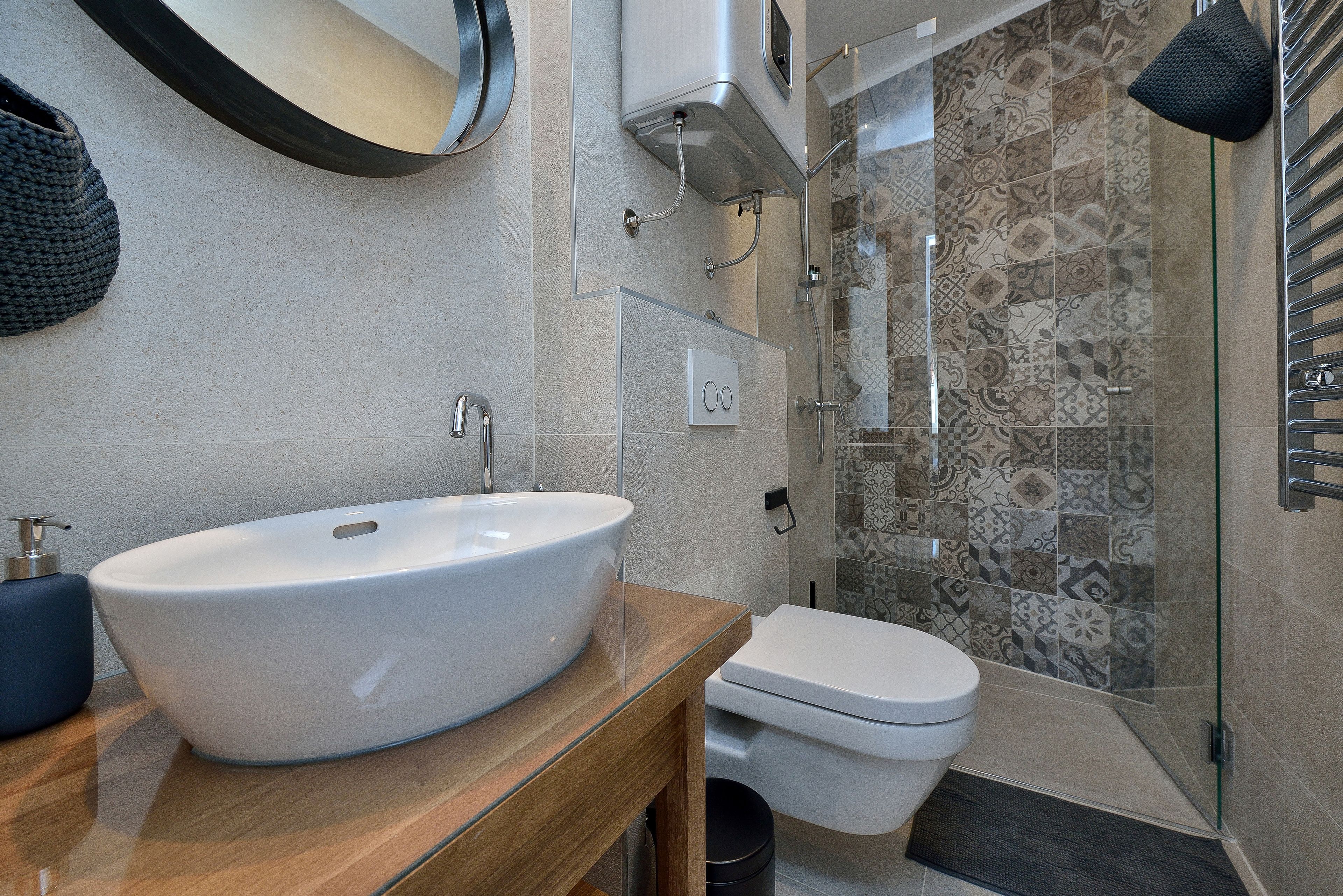 Ein Badezimmer mit einem großen weißen Waschbecken, einer Toilette und einer Dusche mit gemusterten Fliesen.