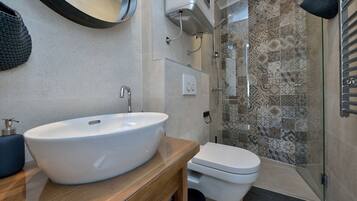 Ein Badezimmer mit einem großen weißen Waschbecken, einer Toilette und einer Dusche mit gemusterten Fliesen.