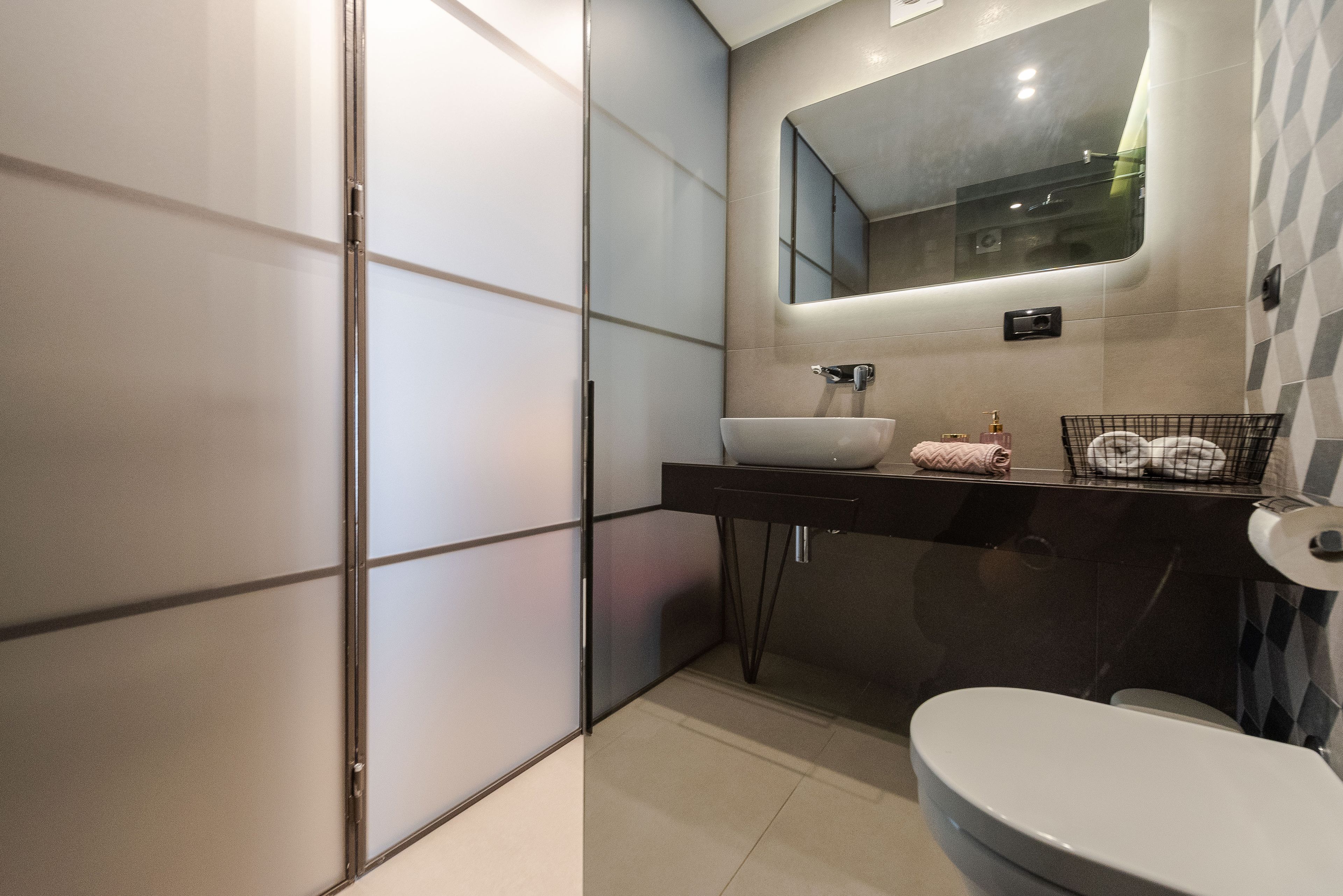 A modern bathroom with a large mirror, a white sink, and a toilet.