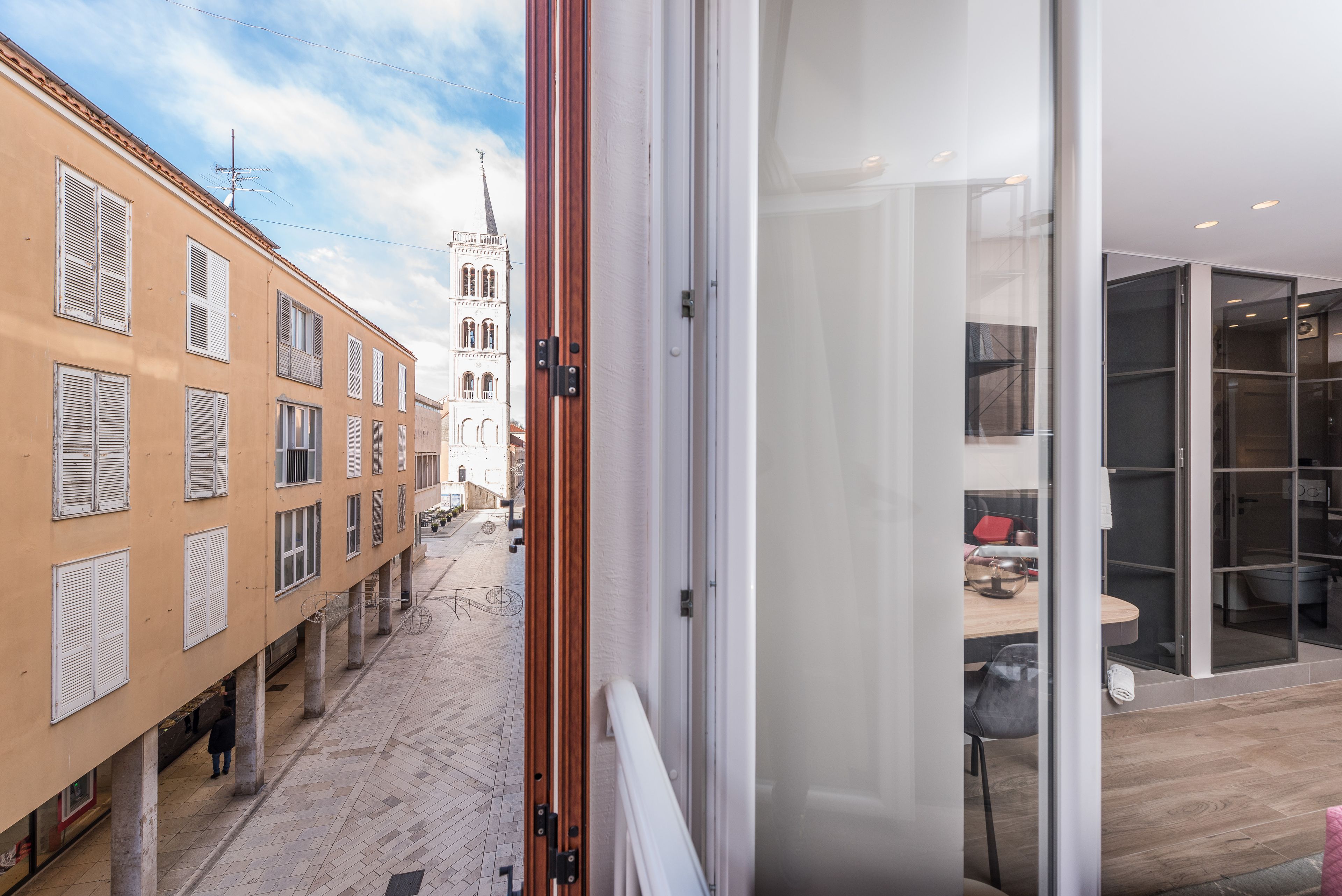 Un interior moderno con un ventanal de vidrio que da a un balcón con vistas a una calle estrecha y edificios históricos.