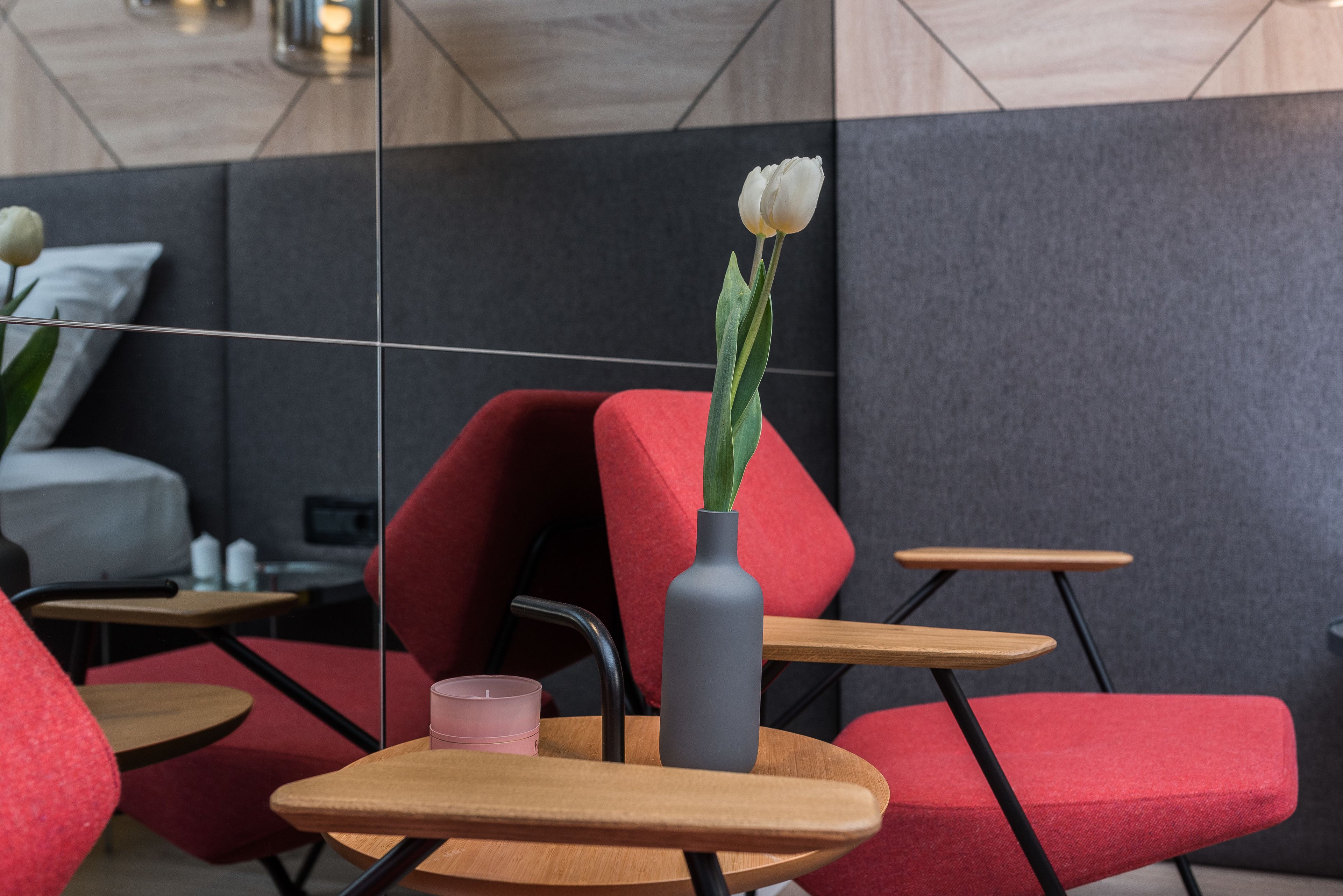 A modern interior with red upholstered chairs, a wooden table, and a grey vase with a white flower.