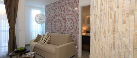 Una sala de estar con un sofá beige, una mesita de centro con revistas y un adornado en la pared.