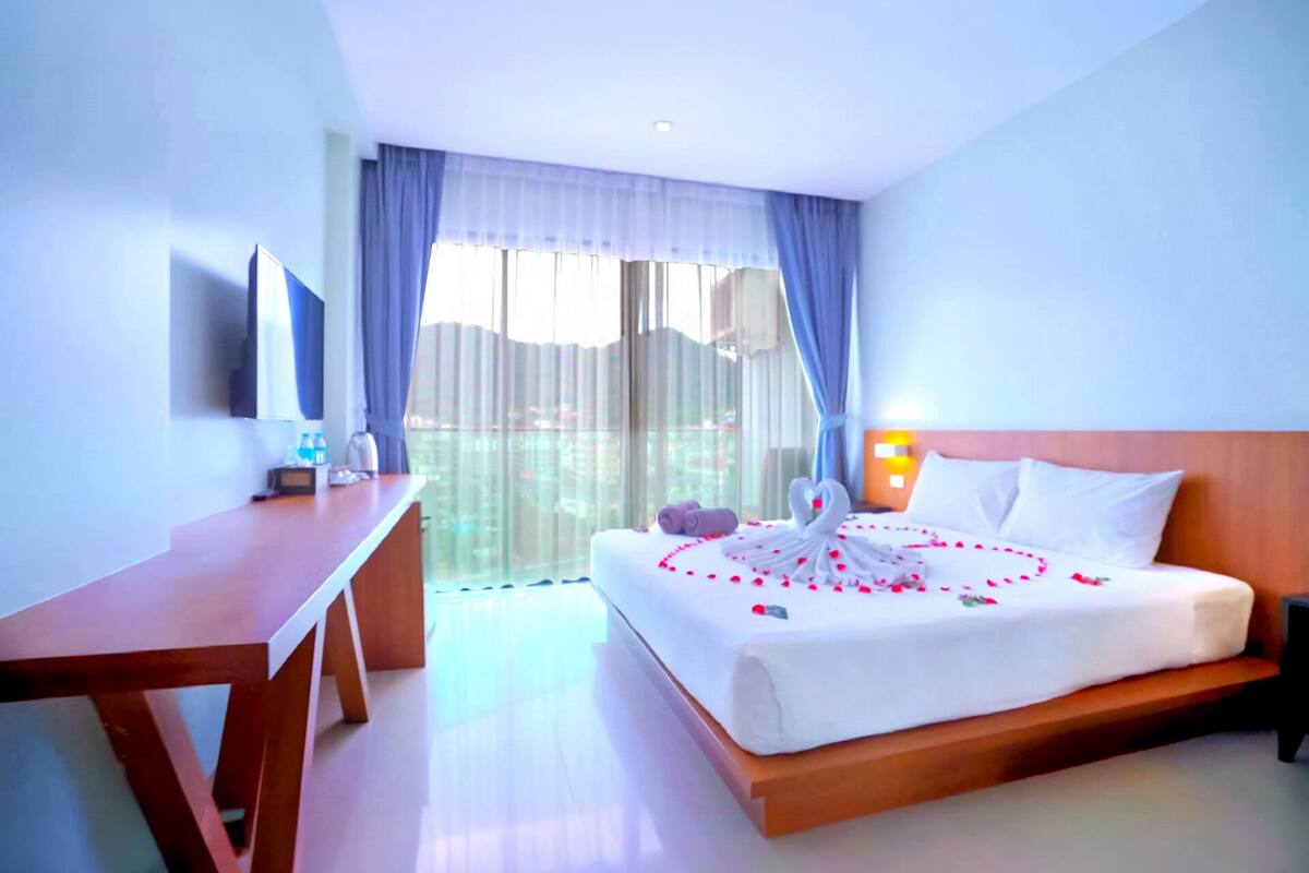A hotel room with a bed, a desk, a chair, a TV, and a window with curtains.