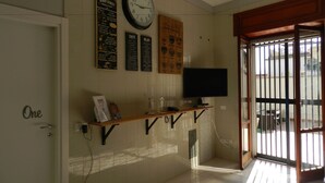 A room with a wall clock, a menu board, a flat-screen TV, and a door labeled "One". - Mola Rooms (Naples)