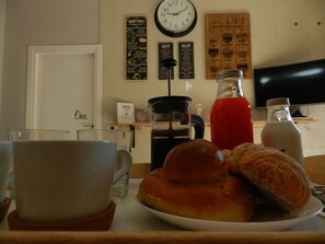 Uma mesa com uma cesta de croissants, uma cafeteira, uma garrafa vermelha de bebida e uma garrafa de leite.