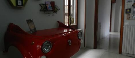 A room with a red car-shaped piece of furniture, a hallway with a door, and a wall with shelves and pictures.