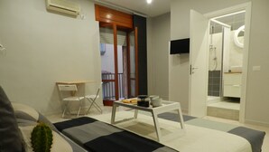 A hotel room with a bed, a small table with a tray of cookies, a potted plant, a chair, and a bathroom visible through an open door. - Mola Rooms (Naples)