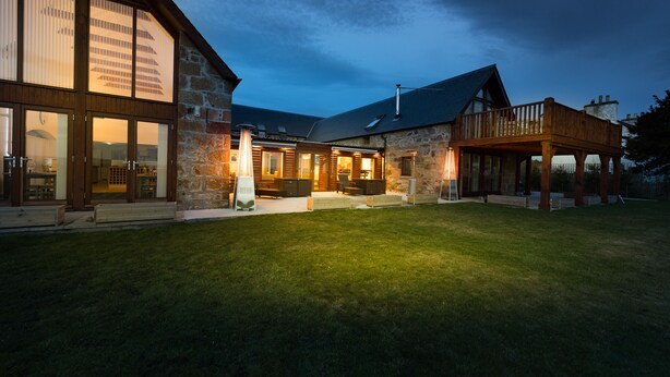 A stone building with a wooden deck and a large glass window. - The Steading (Dornoch)