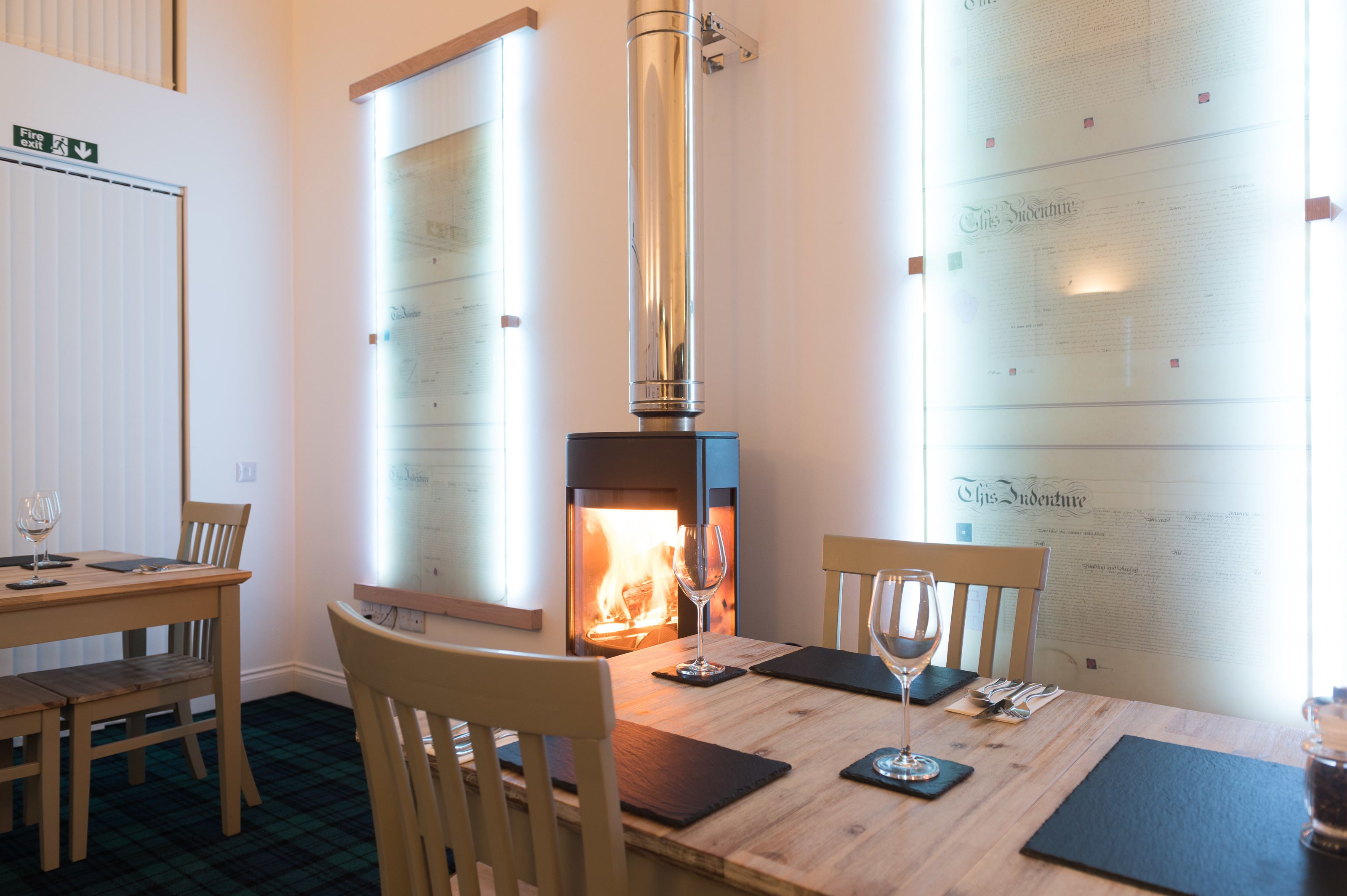 A dining area with a wood-burning stove, a table set for two with wine glasses, and a menu on the wall.