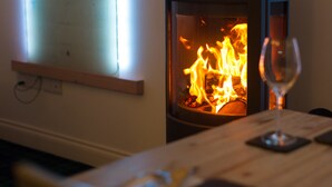 A room with a fireplace, a wooden table, and a wine glass. - The Steading (Dornoch)