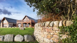 A stone wall with a wooden deck, a stone building with a sloped roof, and a grassy area. - The Steading (Dornoch)