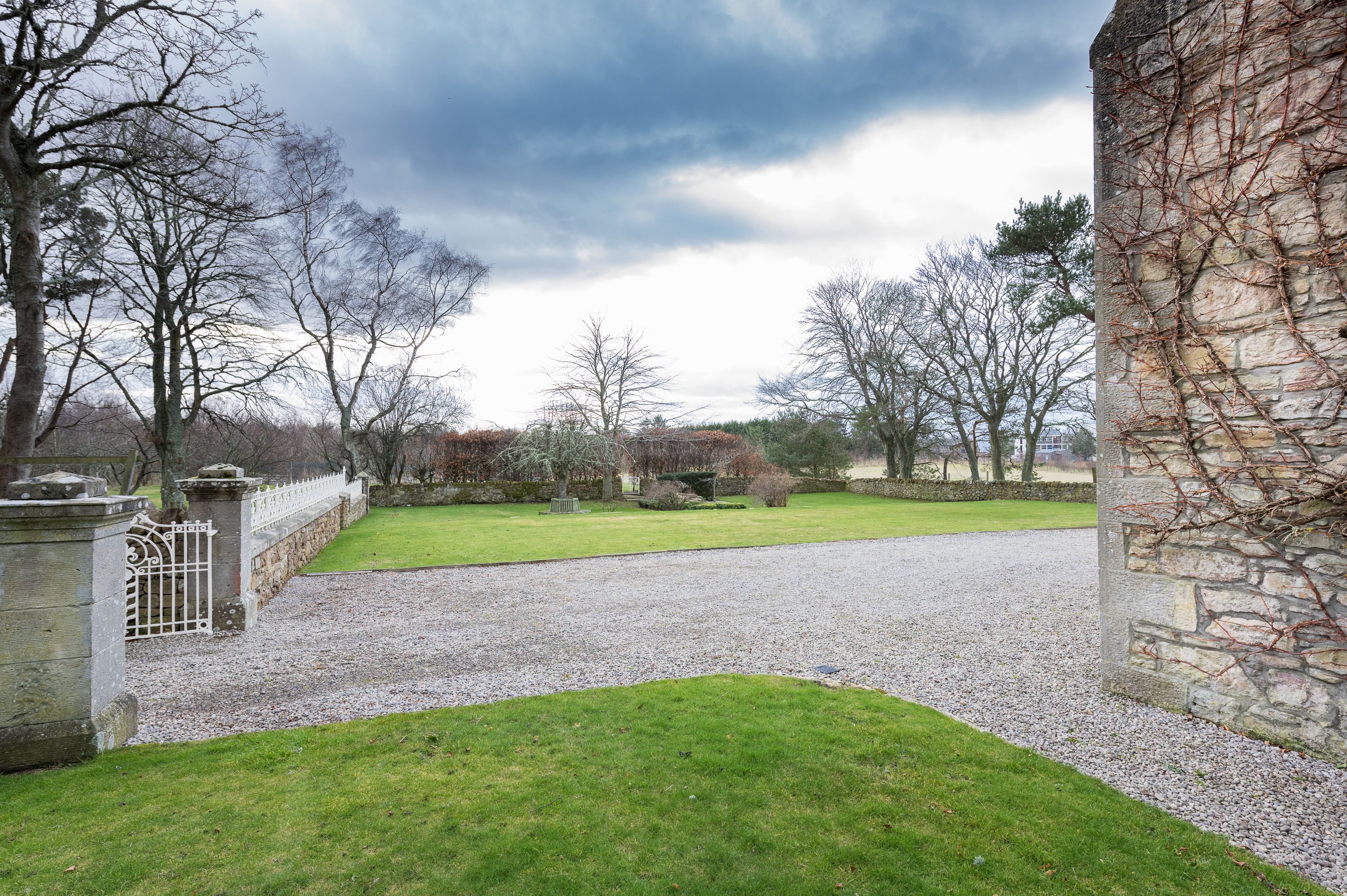 A gravel driveway leading to a stone wall with a metal gate.