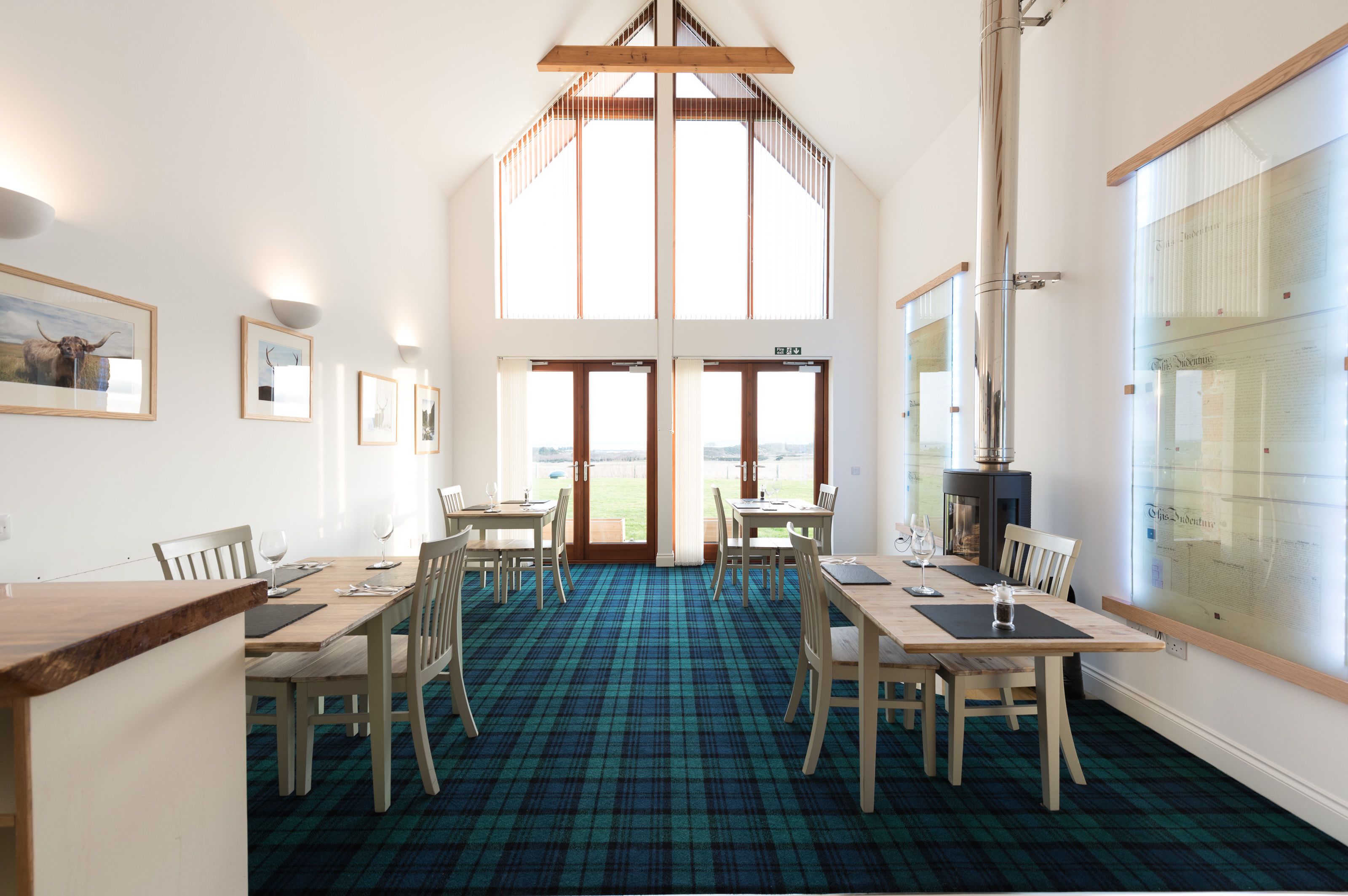 A dining area with a high ceiling, large windows, and a plaid carpet.