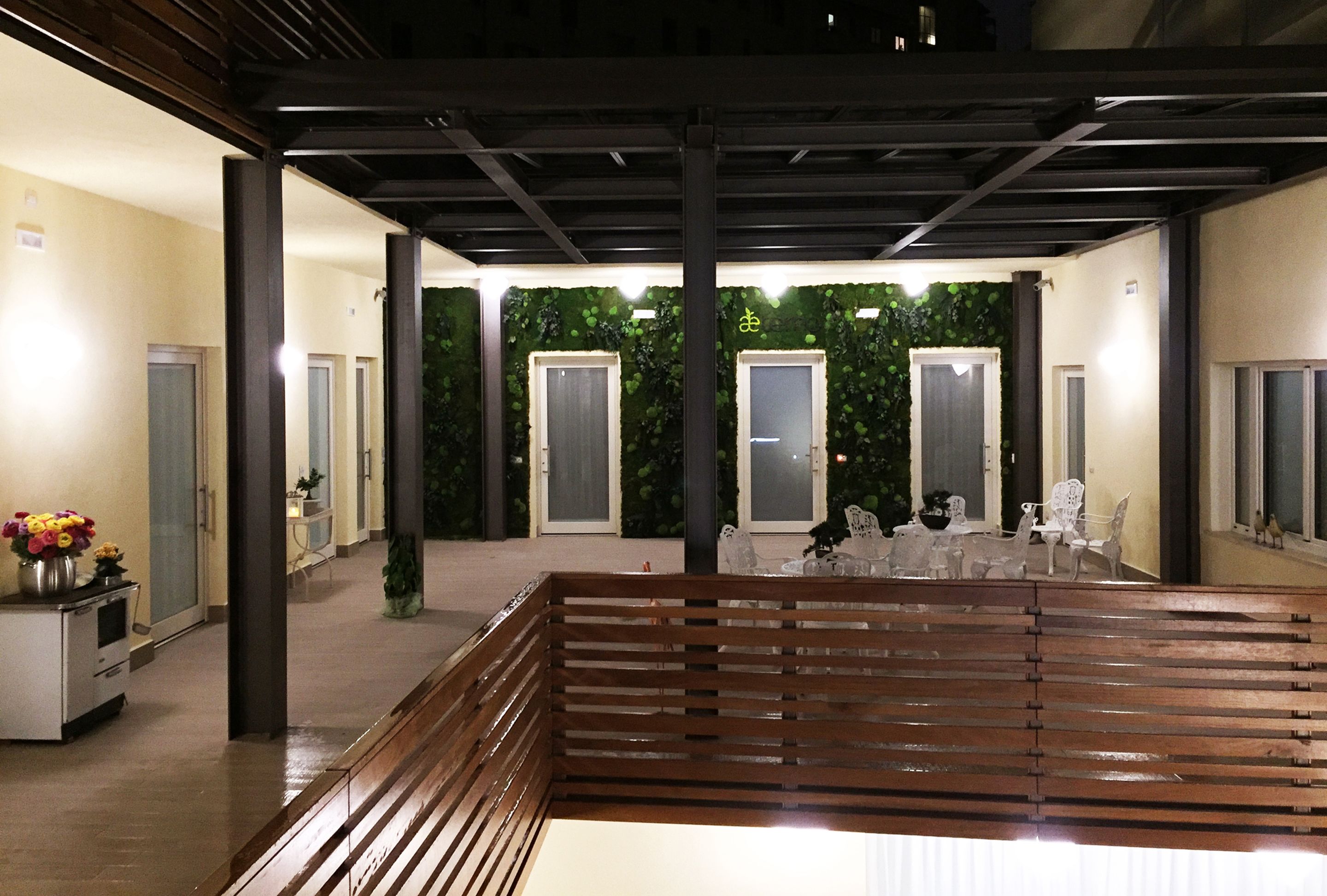 Un espace extérieur abrité avec un banc en bois, un comptoir d’accueil agrémenté d’un vase de fleurs et un mur végétal.