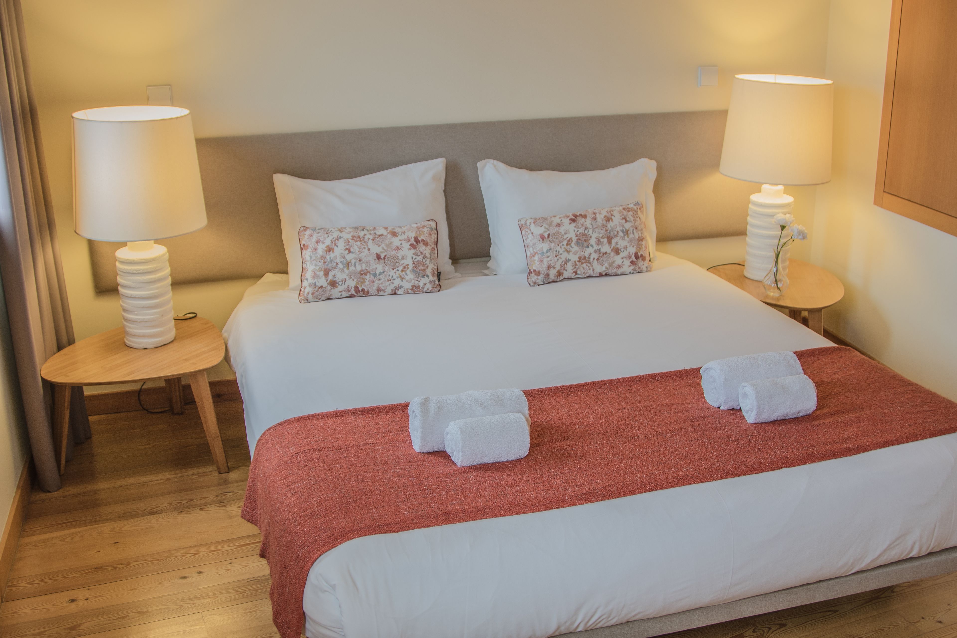 Une chambre d’hôtel avec un grand lit, deux tables de chevet avec des lampes et un plaid rouge.