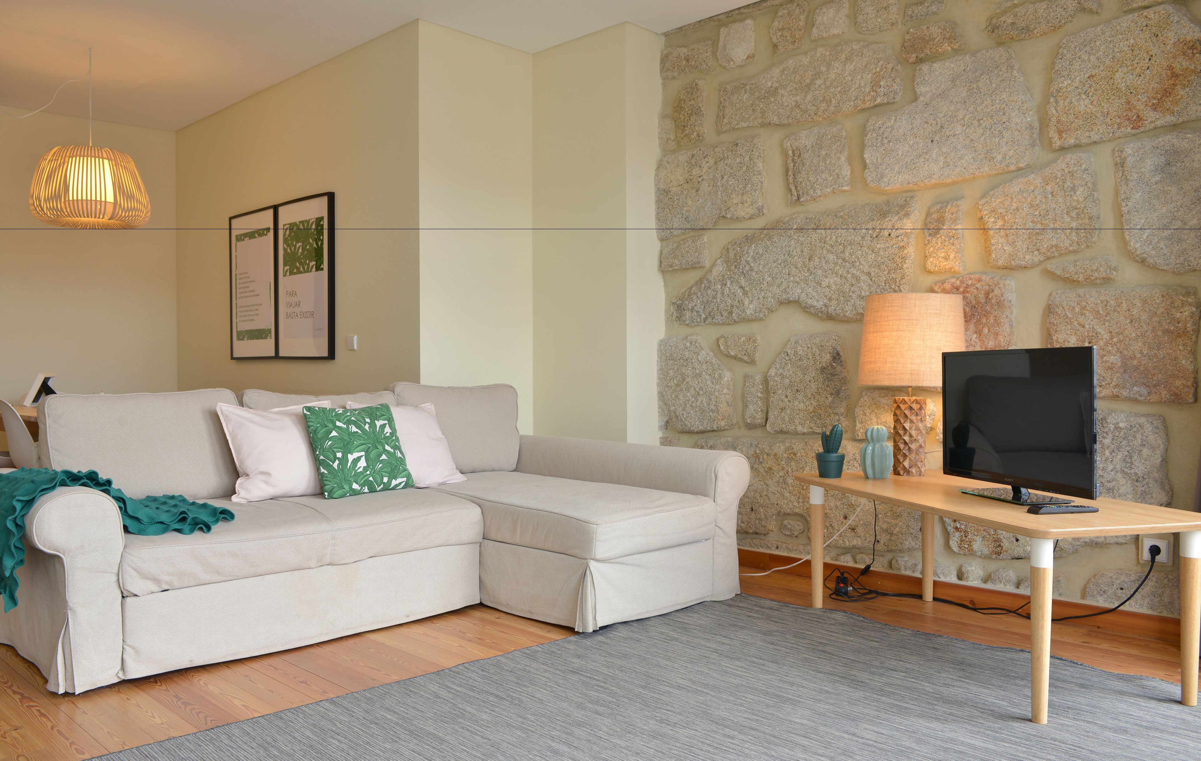 A living room with a beige sofa, a wooden coffee table, a TV, a stone wall, and a hanging light fixture.