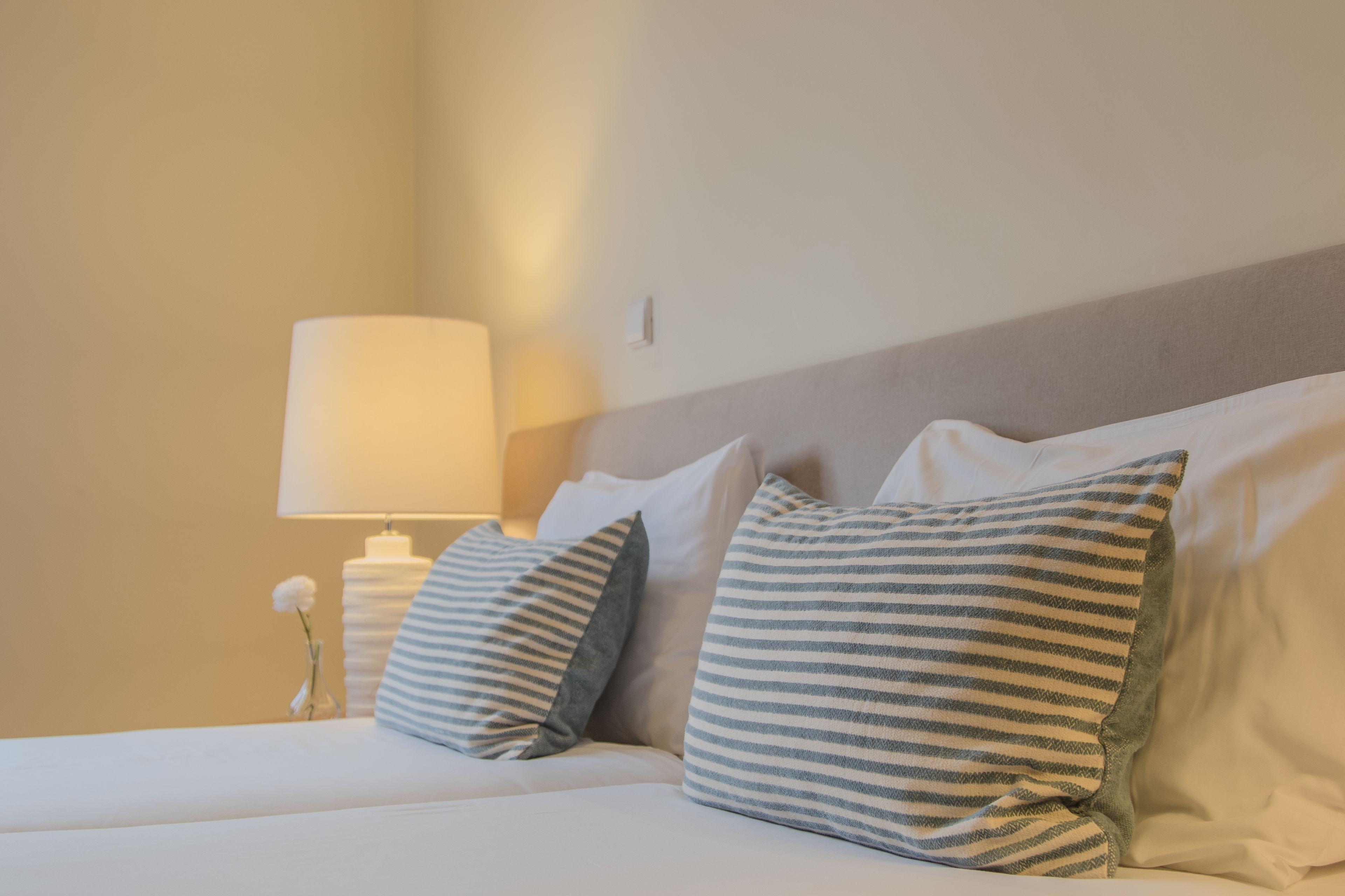 A neatly made bed with striped pillows and a bedside lamp.